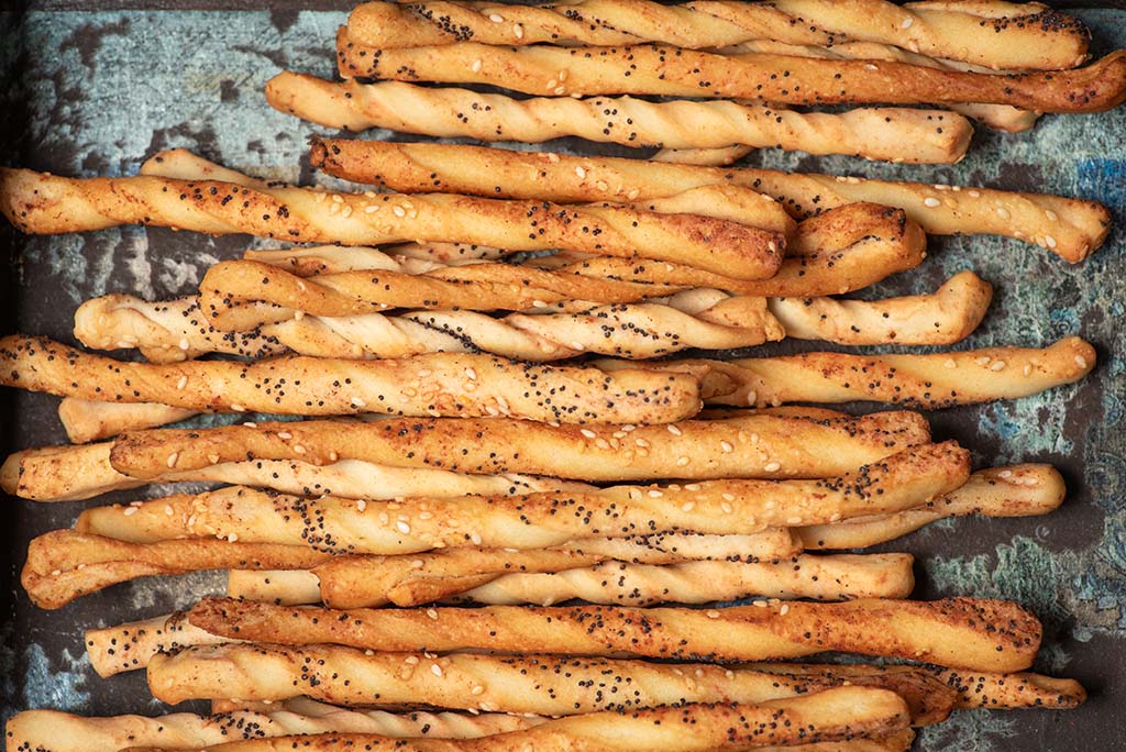 Popcorn-studded breadsticks in rustic wooden tray.